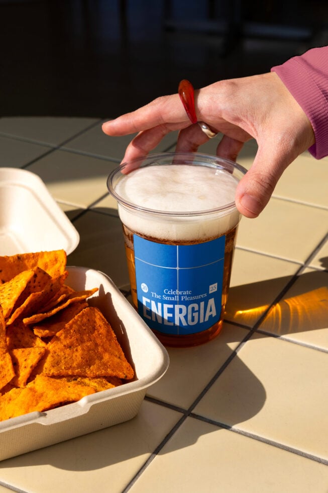 Hand with red nail polish holding Energia cola cup beside food tray