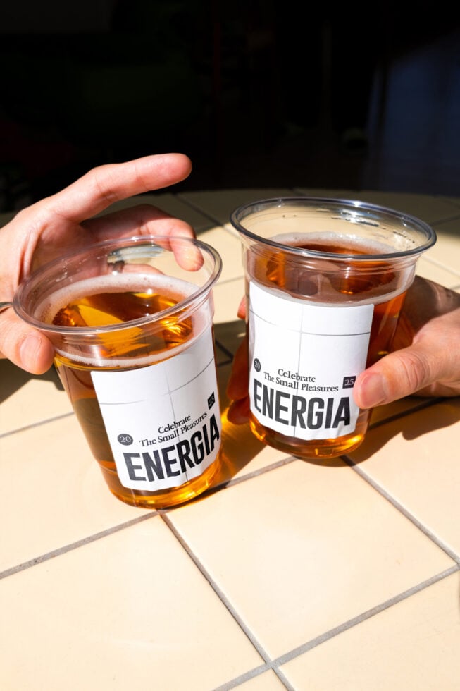 Two cola cups with white blank labels held in hands on tile floor