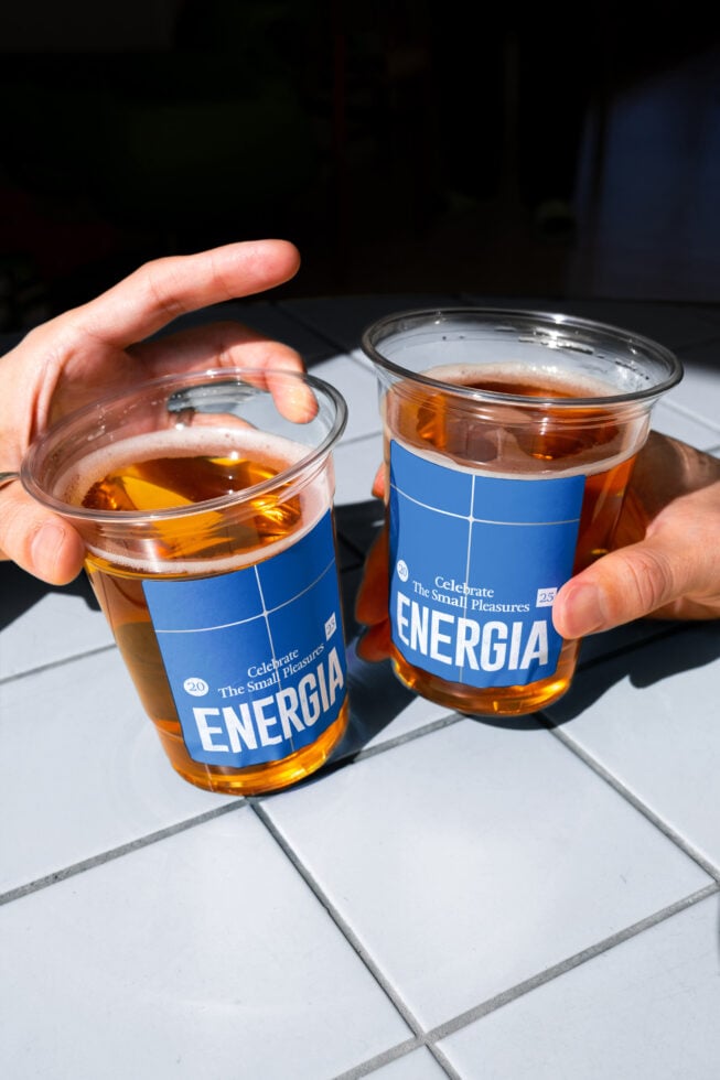 Hands holding two cola cups with blue Energia label on white tiles