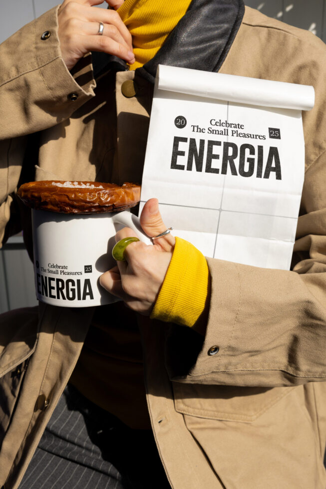 Hands holding white paper bag roll, white cup with pastry showing Energia label mockups