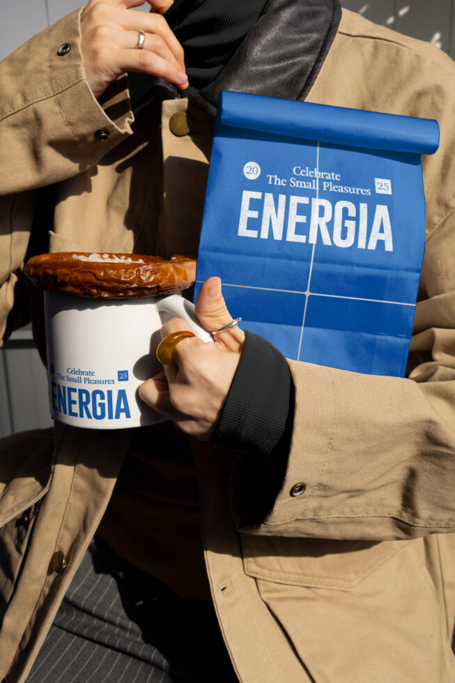 Hands holding white cup, blue paper bag roll, showing Energia branding on both items