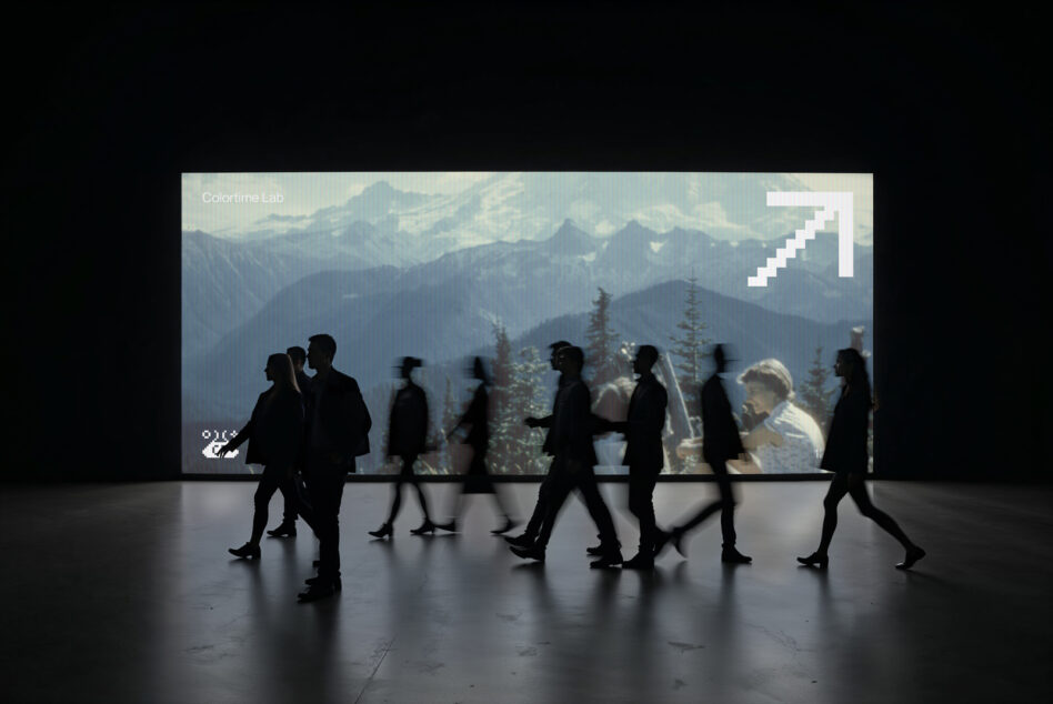 Blurred figures walking past digital screen showing mountain landscape with arrow graphic