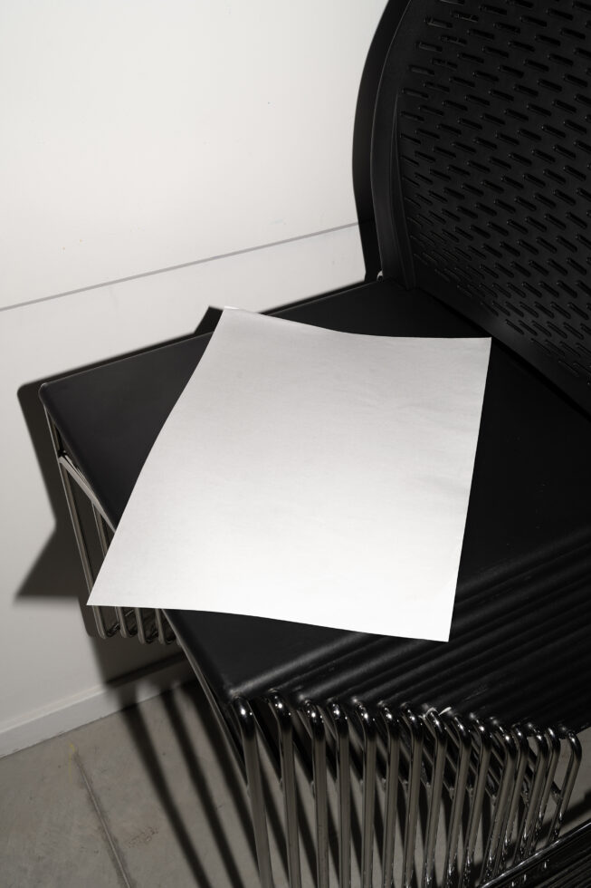 Blank A-size print mockup on black modern chair, minimal white background