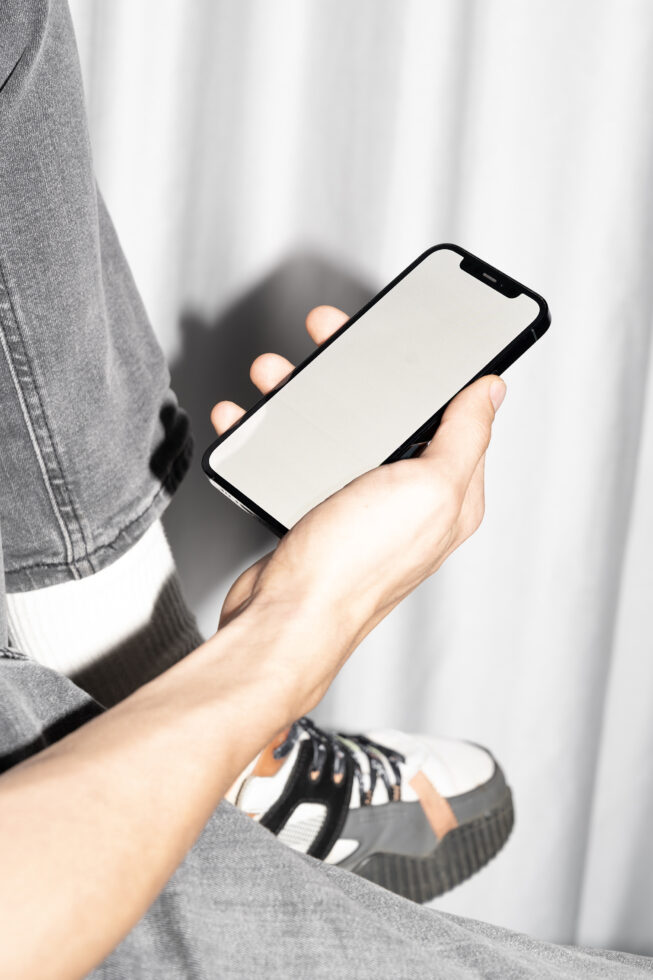 Person in denim jacket holding phone with blank white screen outdoors
