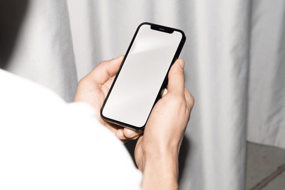 Blank smartphone screen held in both hands against white curtain backdrop