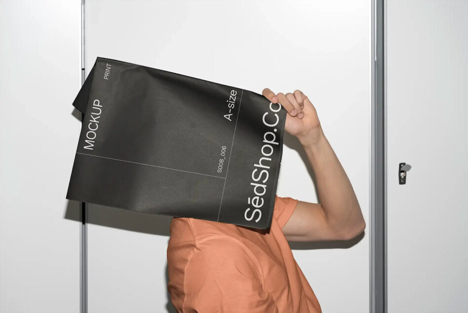 Person holding black A4 folder mockup with white text against white door frame background