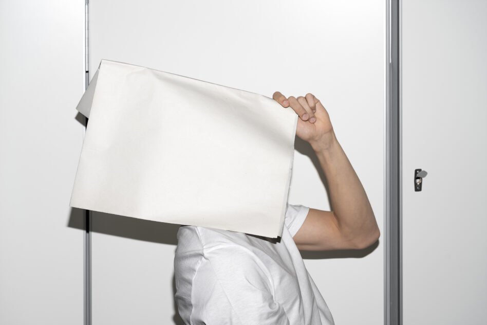 Person holding blank white A4 document sheet in front of white minimalist door frame