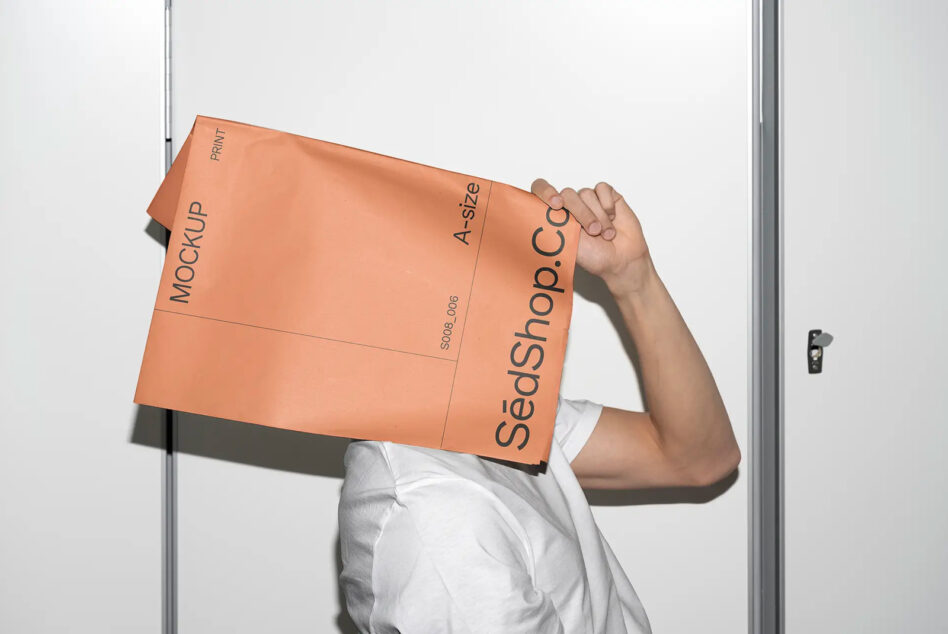 Person holding orange A4 folder mockup with black text against white door frame background