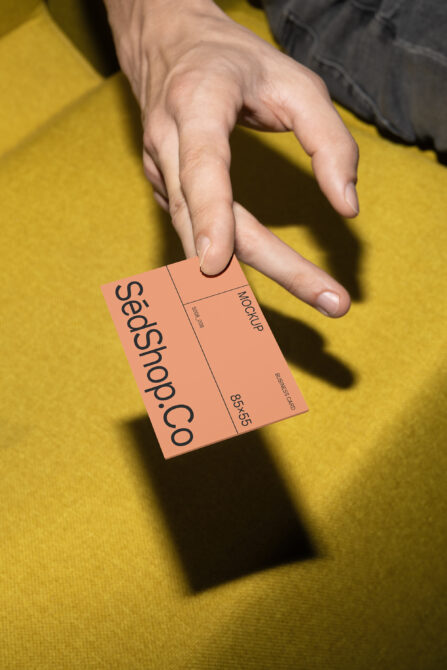 Hand displaying coral orange folded business card mockup on yellow surface