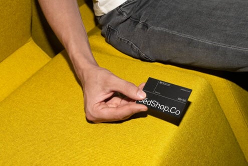 Hand holding black business card mockup on bright yellow furniture