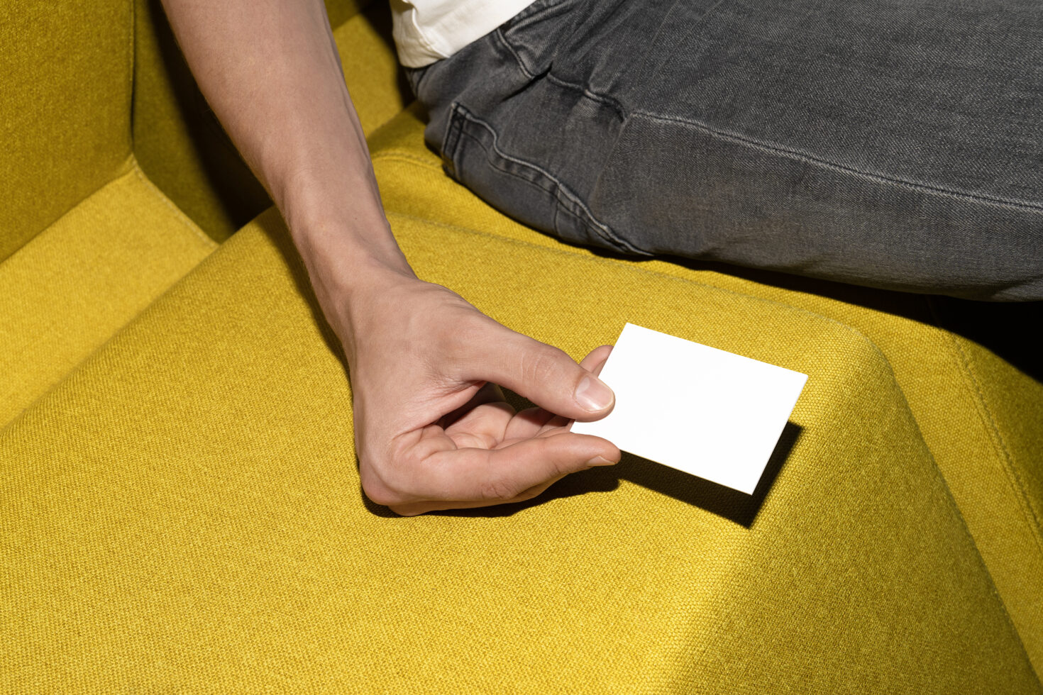 Hand holding blank white business card on mustard yellow couch