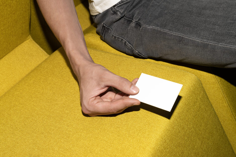 Hand holding blank white business card on mustard yellow couch
