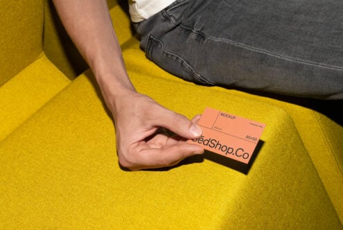 Person holding coral orange business card mockup on yellow fabric