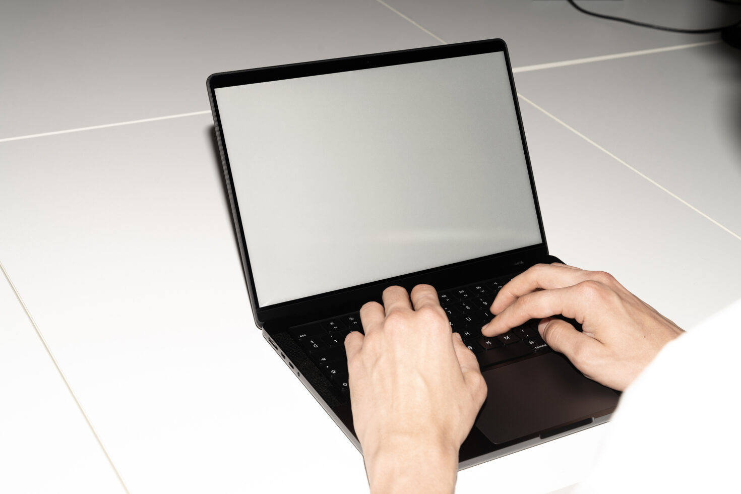 Hands typing on black laptop with blank screen displayed on yellow desk