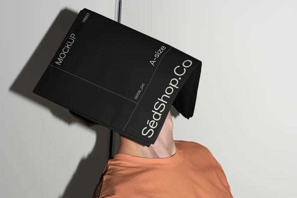 Person in orange shirt holding black A2 SedShop.Co mockup as head cover