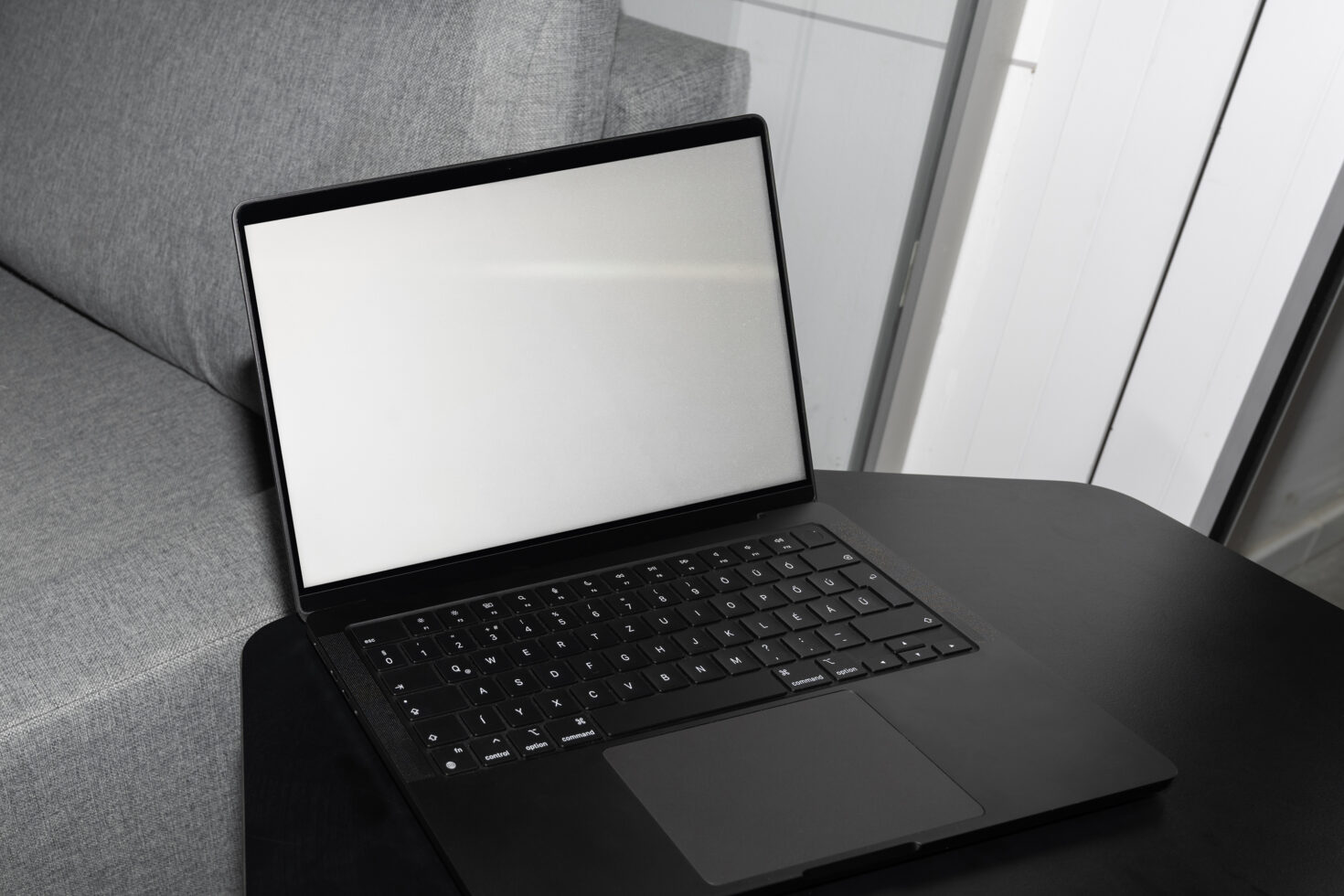 Black laptop on couch showing blank white screen display with keyboard visible
