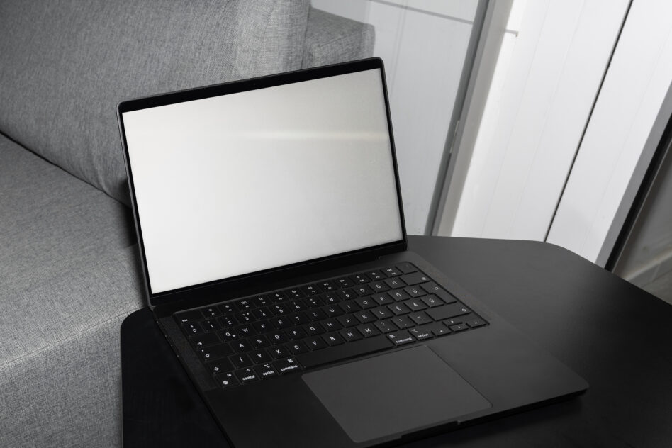 Black laptop on couch showing blank white screen display with keyboard visible