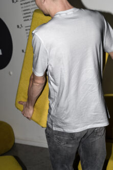 Person wearing white t-shirt holding yellow folder, back view