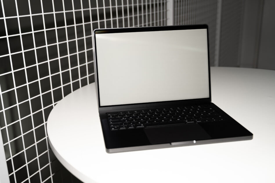 Laptop on white table with blank screen, geometric grid wall backdrop