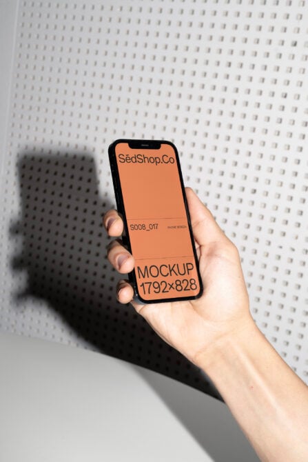 Hand holding black iPhone showing SedShop.Co orange screen mockup against textured wall