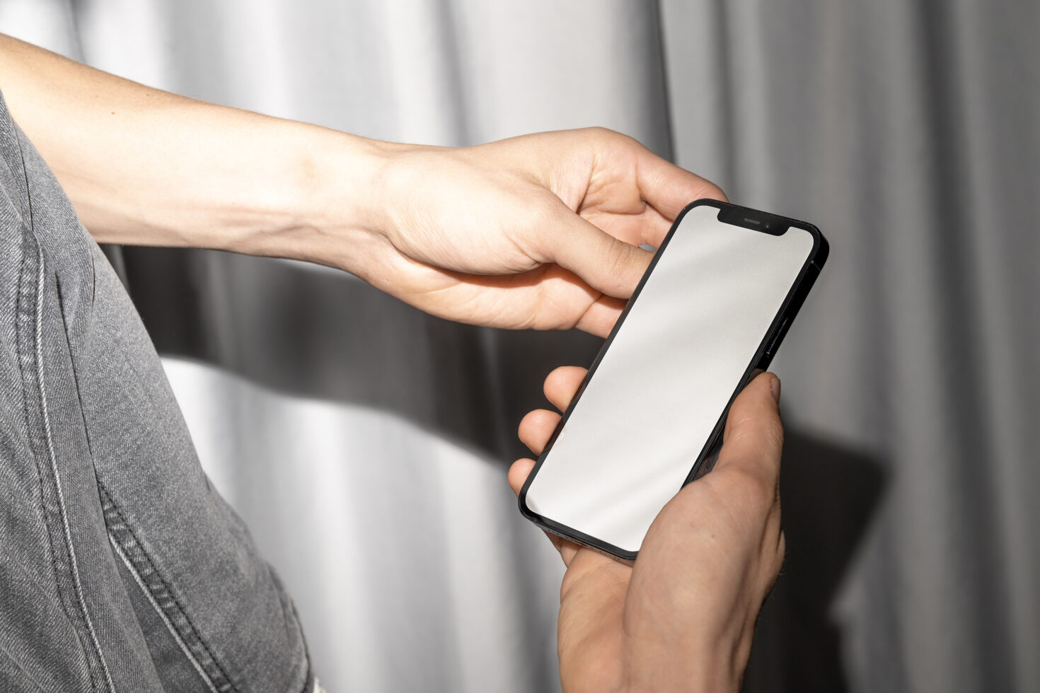 Person in gray jacket holding black iPhone with blank white screen, natural lighting
