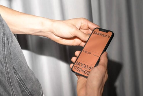 Person in gray shirt holding black iPhone with warm orange screen display mockup
