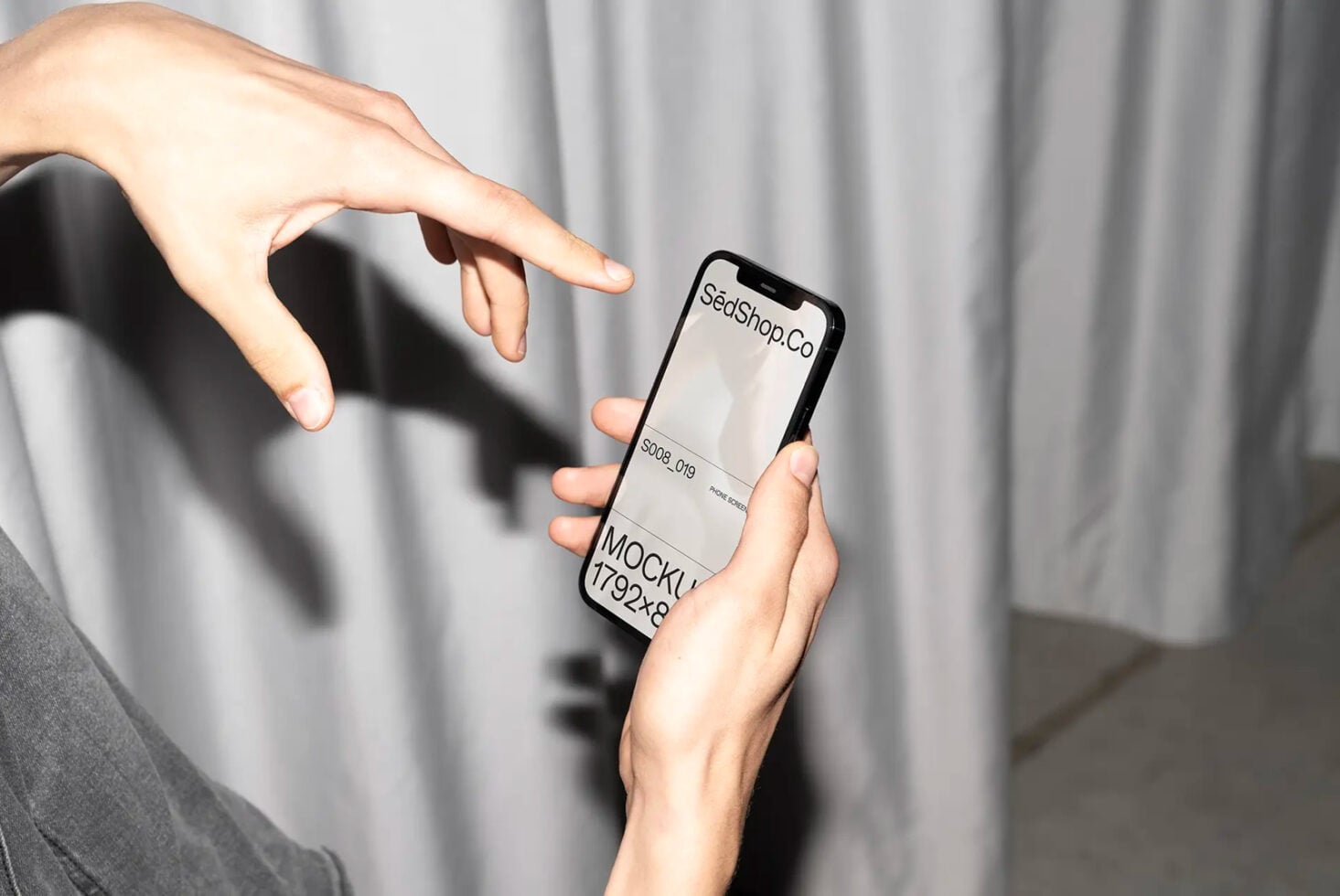Hands holding black iPhone displaying SedShop.Co branding in neutral tones