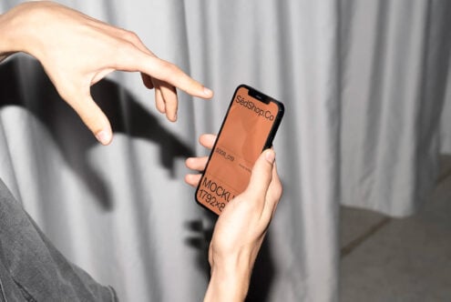 Hands holding black iPhone with warm orange screen showing SedShop.Co mockup