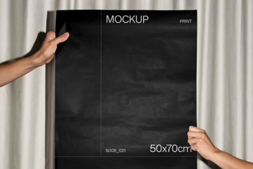 Hands holding black poster with white mockup text against cream curtain