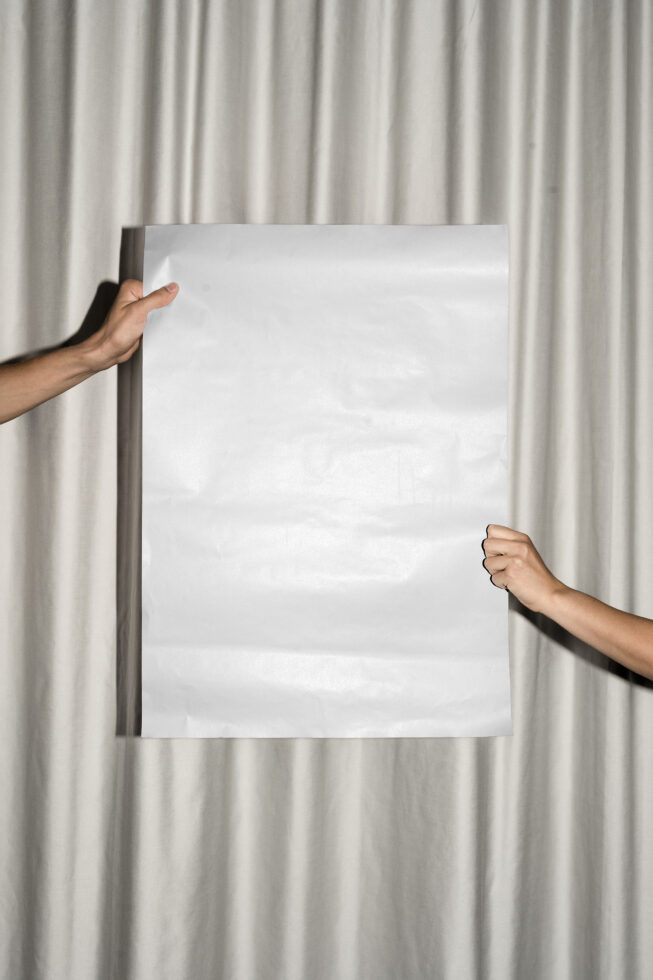 Hands holding blank white poster against pleated cream curtain backdrop