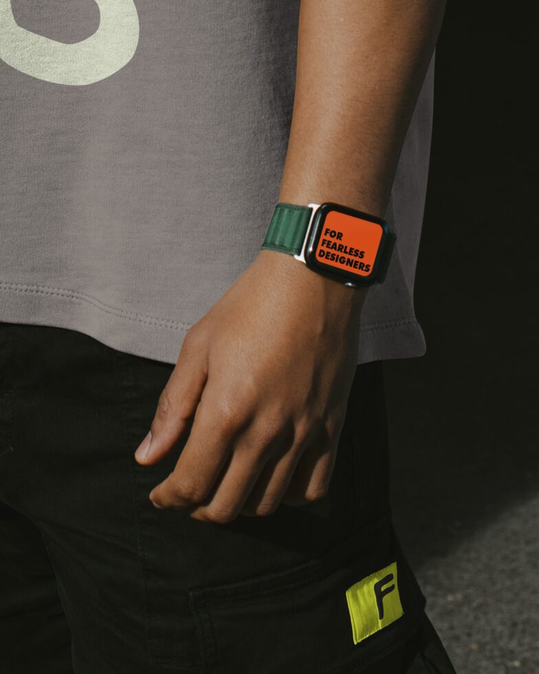 Wrist wearing smartwatch with green band orange face text on gray tee