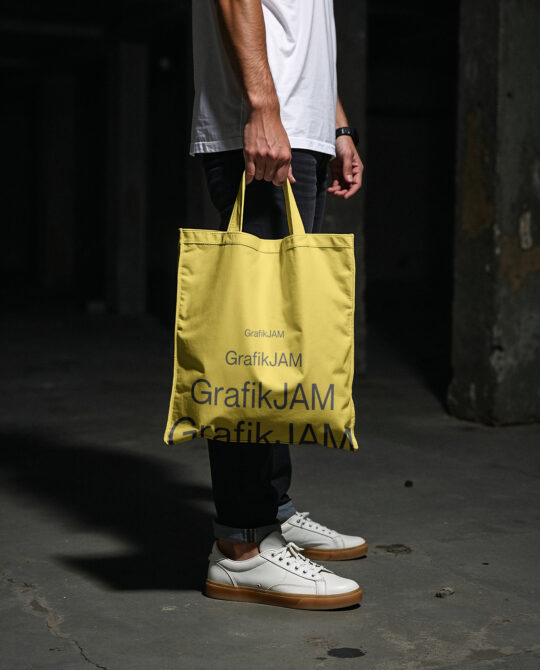 Yellow tote bag with repeated text design in hands of figure