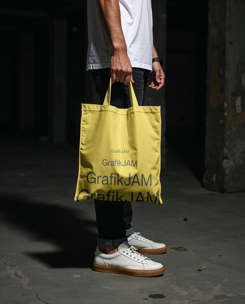 Yellow tote bag with repeated text design in hands of figure