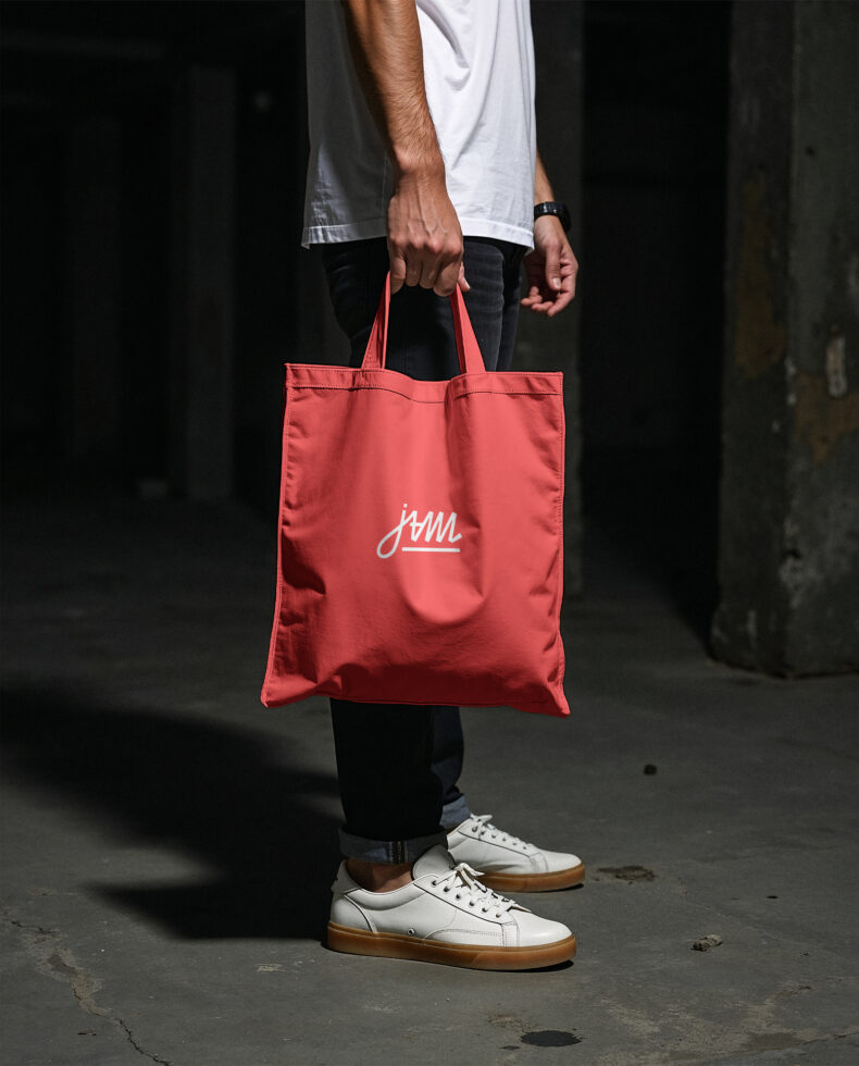 Red tote bag with script logo held by person in white sneakers
