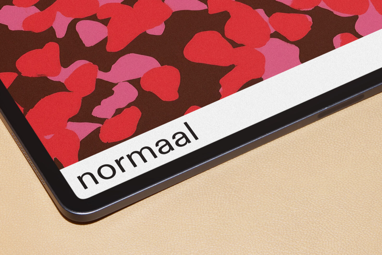 Tablet showing red floral pattern with normaal branding label on beige surface