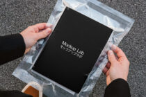 Black book in clear plastic wrapper being held up outdoors on pavement