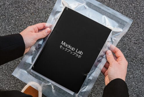 Black book in clear plastic wrapper being held up outdoors on pavement