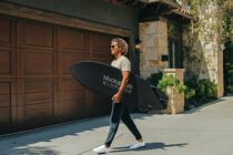 Cyclist holding black surfboard mockup in front of wooden garage