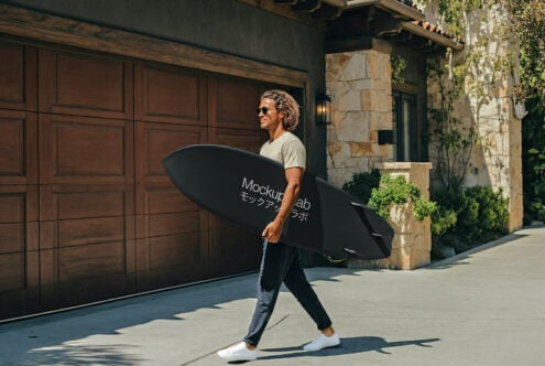 Cyclist holding black surfboard mockup in front of wooden garage