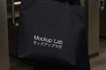 Black tote bag with white text mockup held by handles