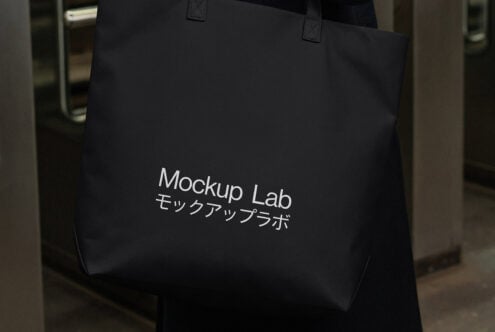 Black tote bag with white text mockup held by handles