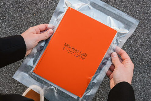 Bright orange book in plastic packaging held in hands against concrete