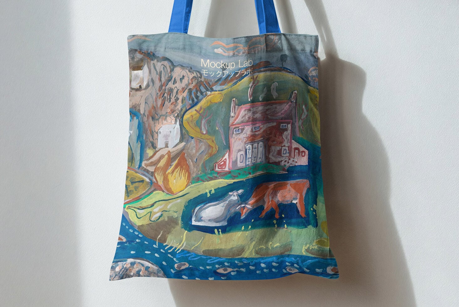 Blue handled tote bag hanging on wall showing painted countryside with houses