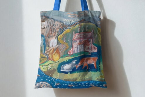 Blue handled tote bag hanging on wall showing painted countryside with houses