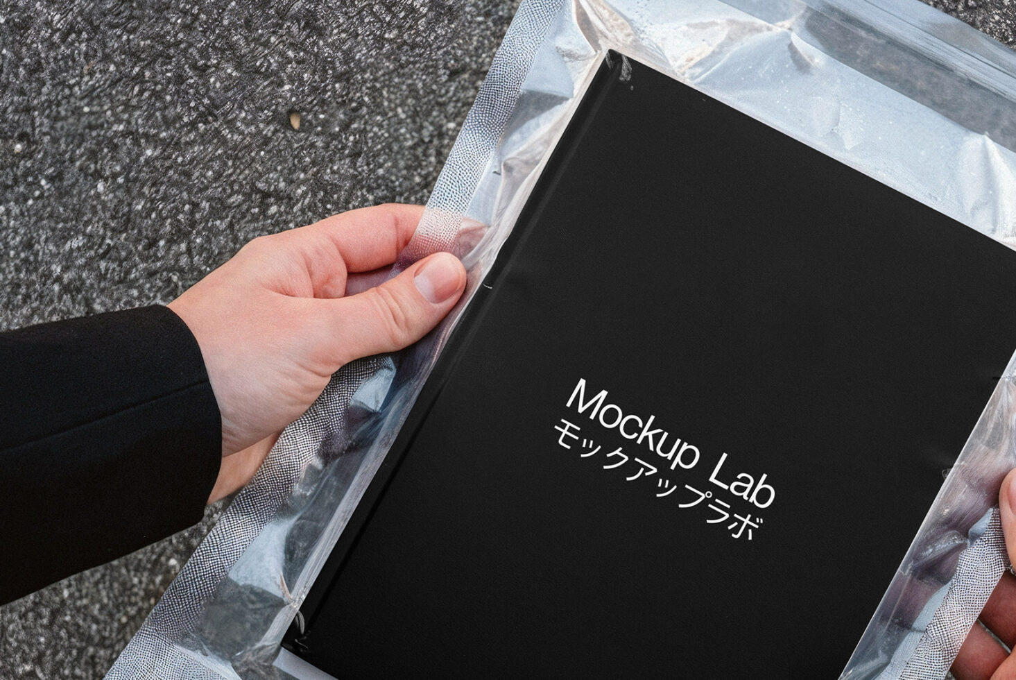 Tablet device mockup in clear plastic packaging held on concrete ground overhead view