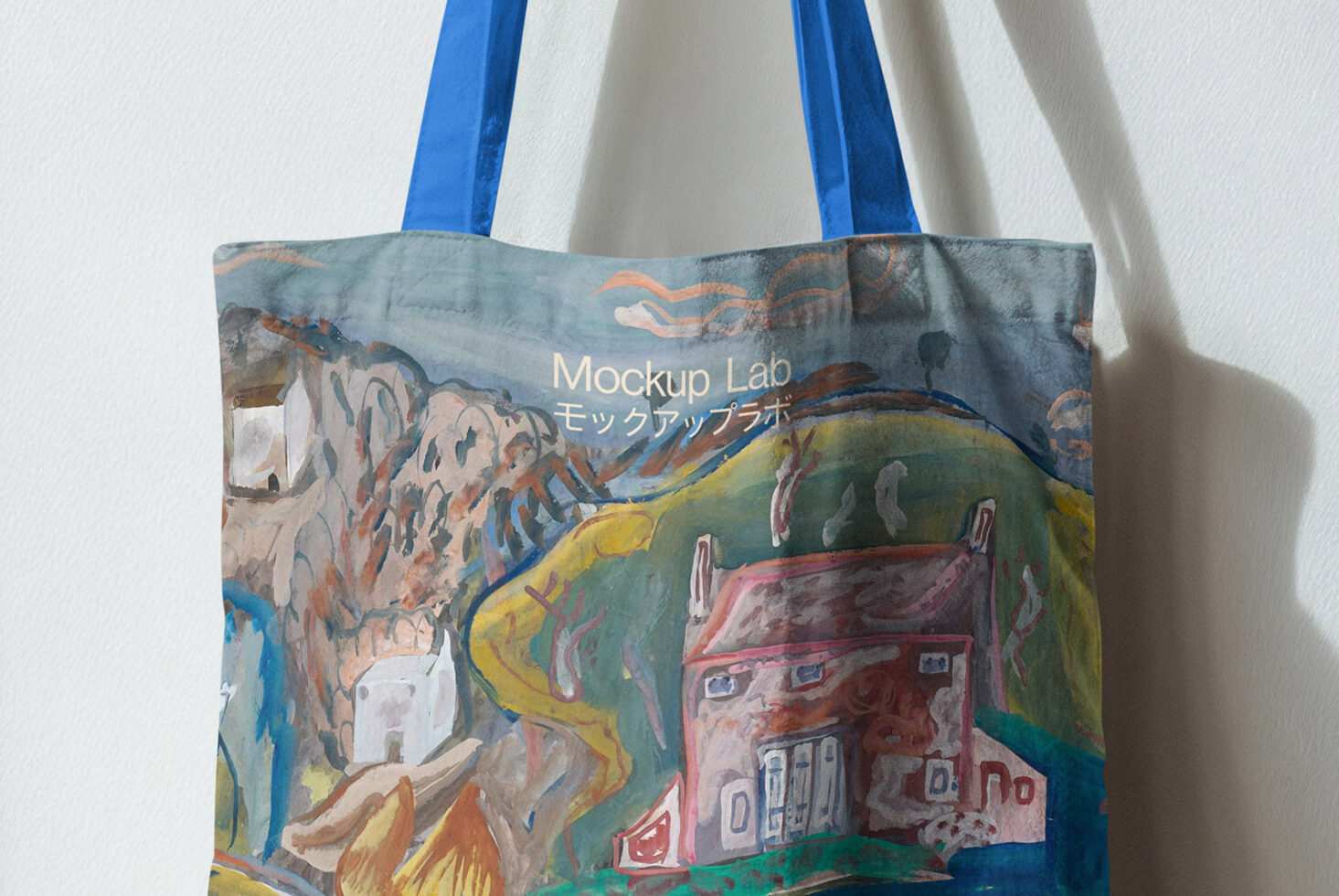 Blue handled tote with colorful landscape illustration of houses, mountains, river