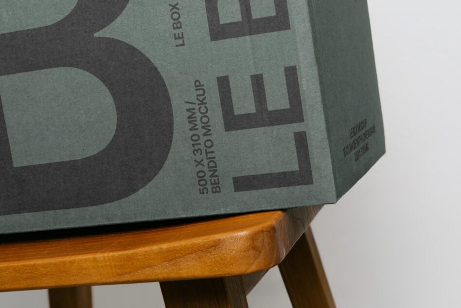 Sage green box mockup with black X logo detail on wooden furniture