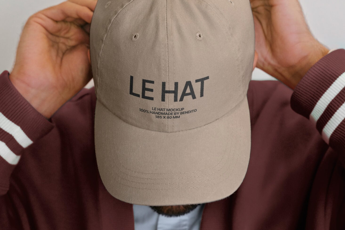 Cream cap front view with LE HAT branding, hands in burgundy hoodie