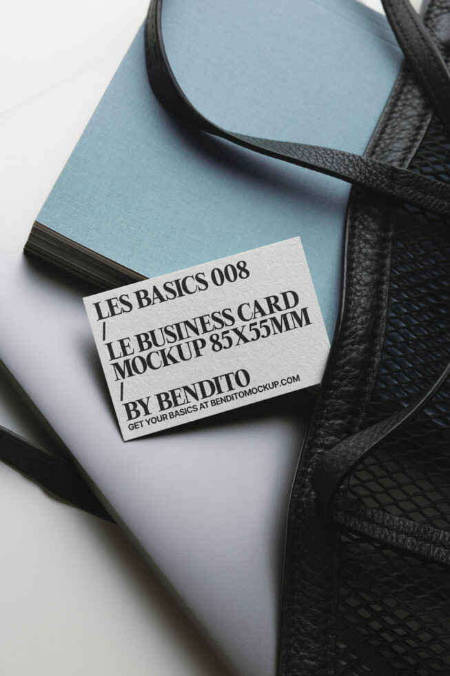Light business card mockup resting on blue notebook next to black leather bag