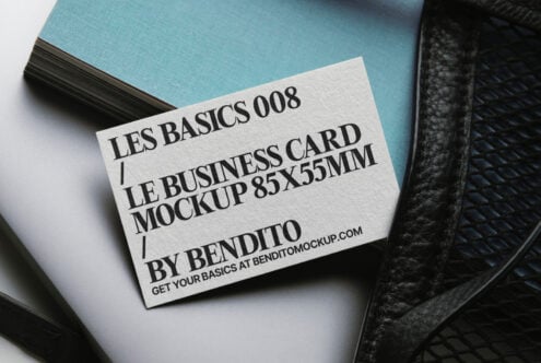 Cream business card on blue notebook stack beside dark leather bag element